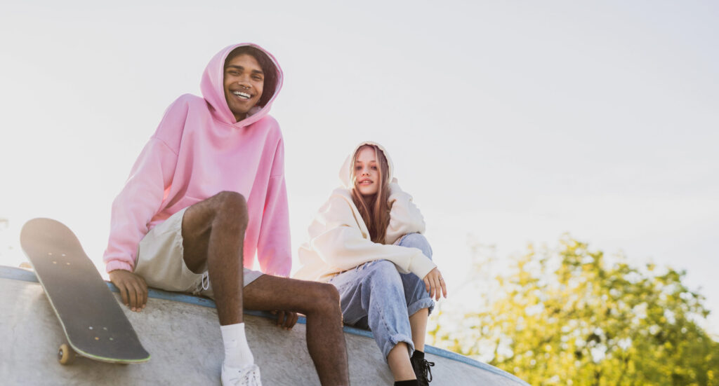 Two stylish multicultural young friends bonding outdoors and having fun at urban skate park.