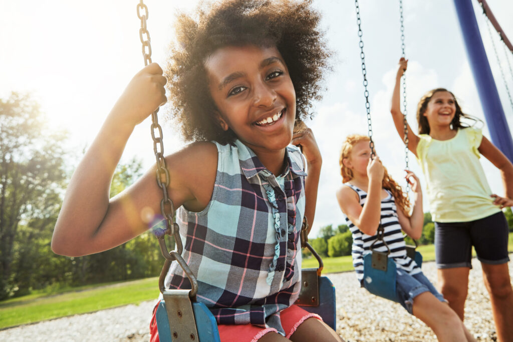 Enjoying the fresh air with friends. Portrait of a young girl playing on a swing at the park with her friends.