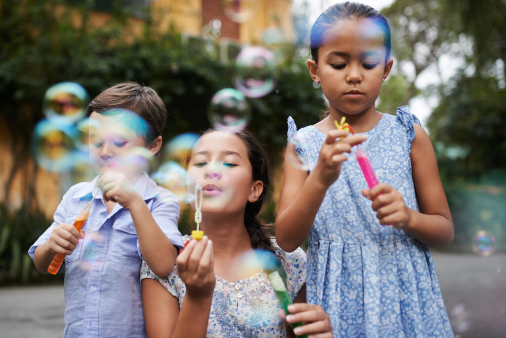 Three young children blowing bubbles outside.