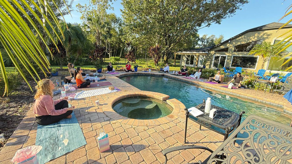 Women meditating on yoga mats around pool.