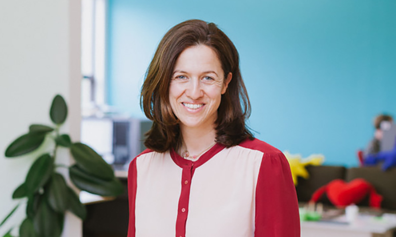 Headshot of Anne-Sophie Brieger in pink/red button sweater in room painted blue.