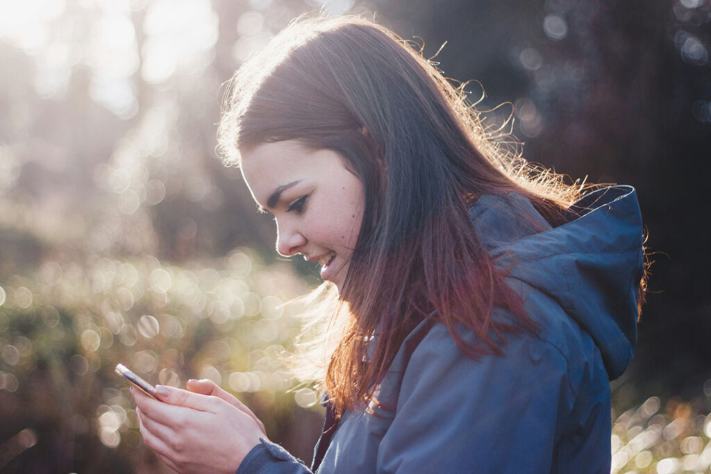 brunette female teenager outside looking down at her cellphone